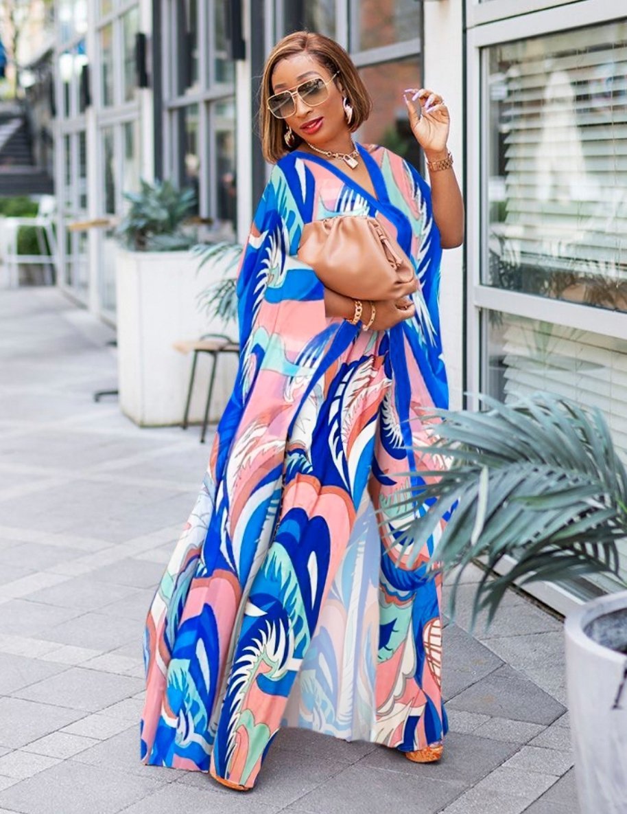 Woman wearing a colorful patterned dress holding a brown handbag on a city street.