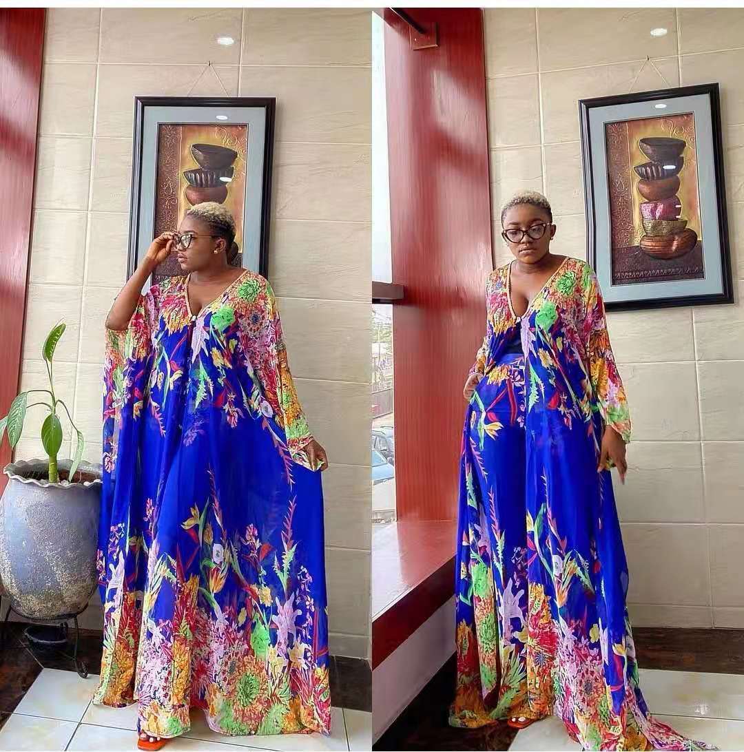 Woman in a colorful dress standing in a room with a tiled wall and framed picture.