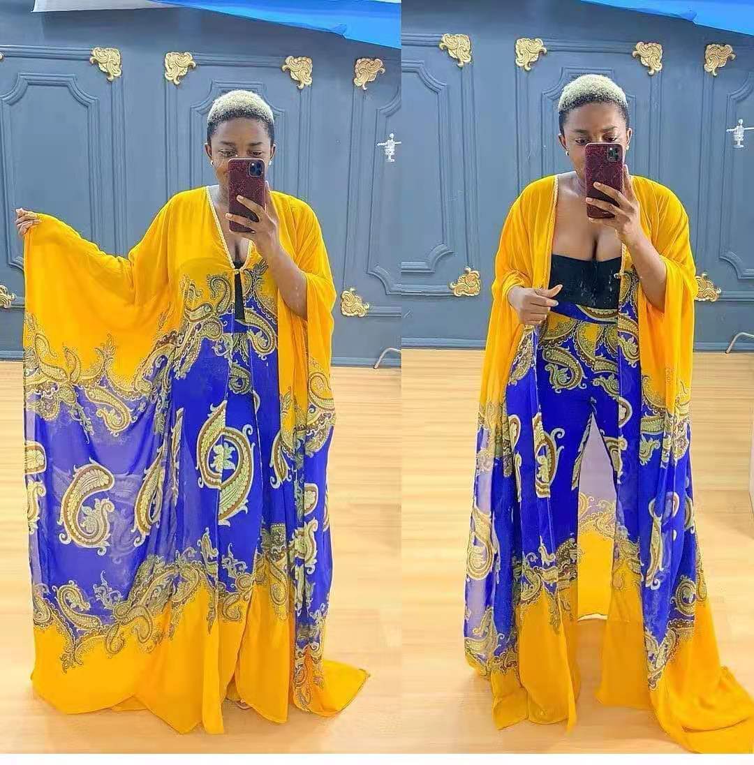 Woman wearing a yellow and blue traditional outfit with intricate patterns, standing in front of a blue wall.
