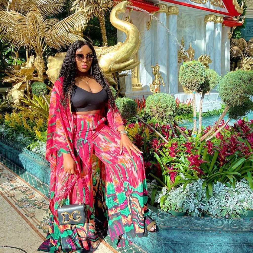 Woman in a colorful outfit standing in front of a decorative fountain with gold sculptures and floral arrangements.
