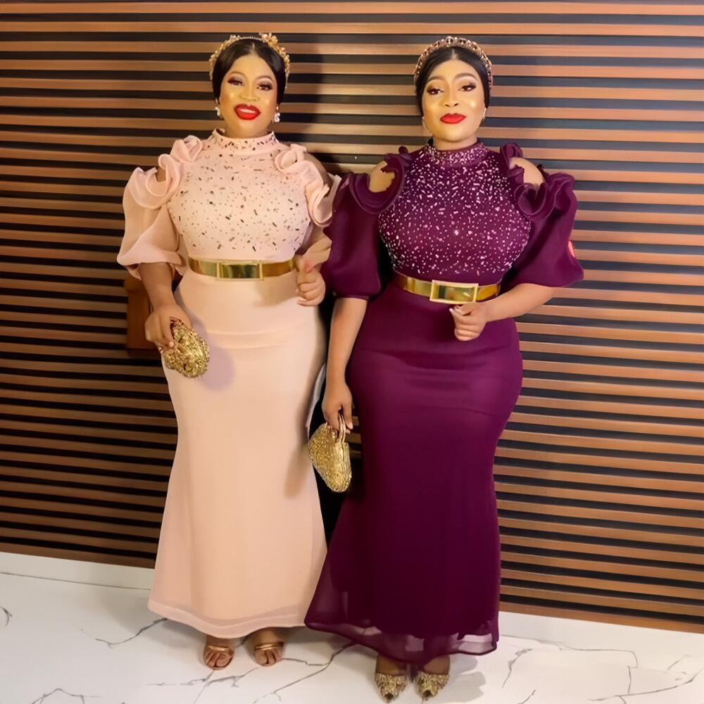 Two women in formal attire standing against a striped wall.