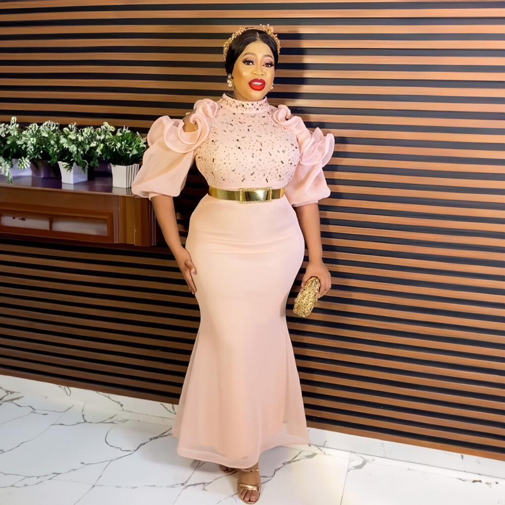 Woman in a pink dress with gold belt standing against a striped wall.