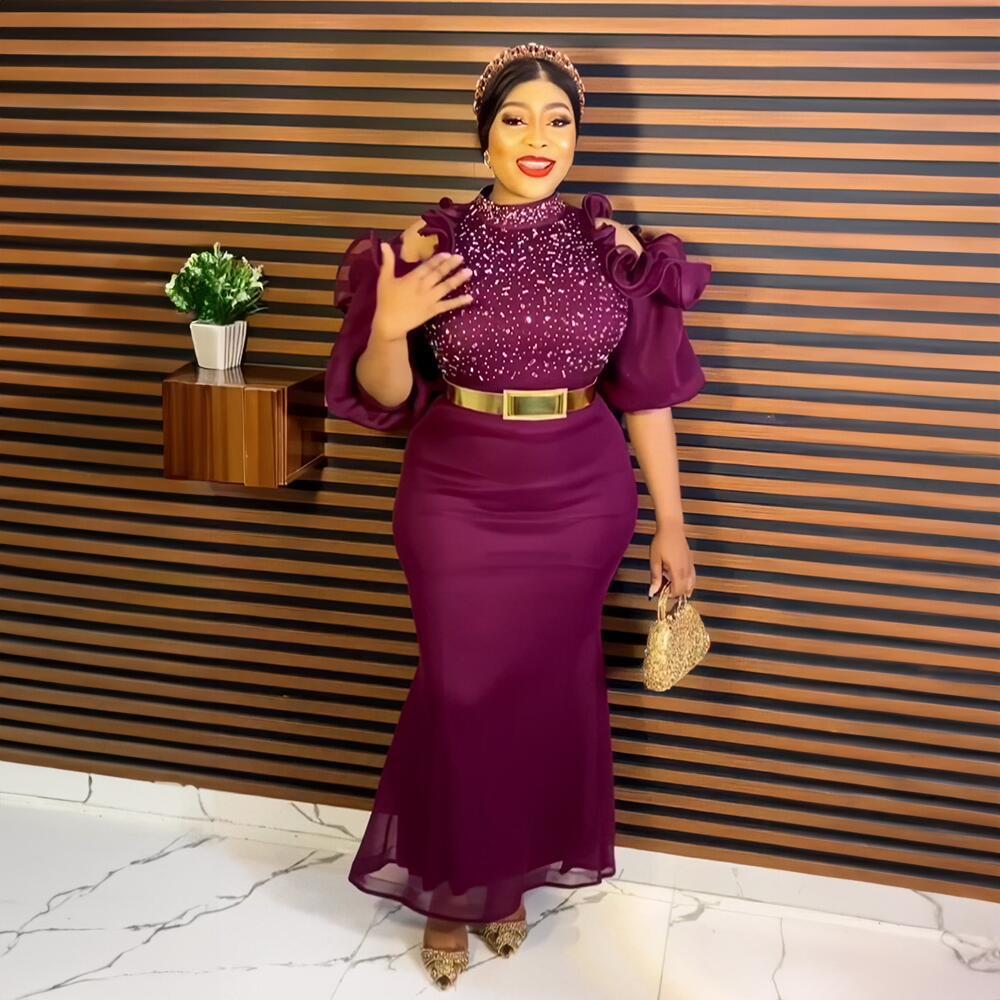 Woman in a purple dress standing against a striped wall with a small table and plant.