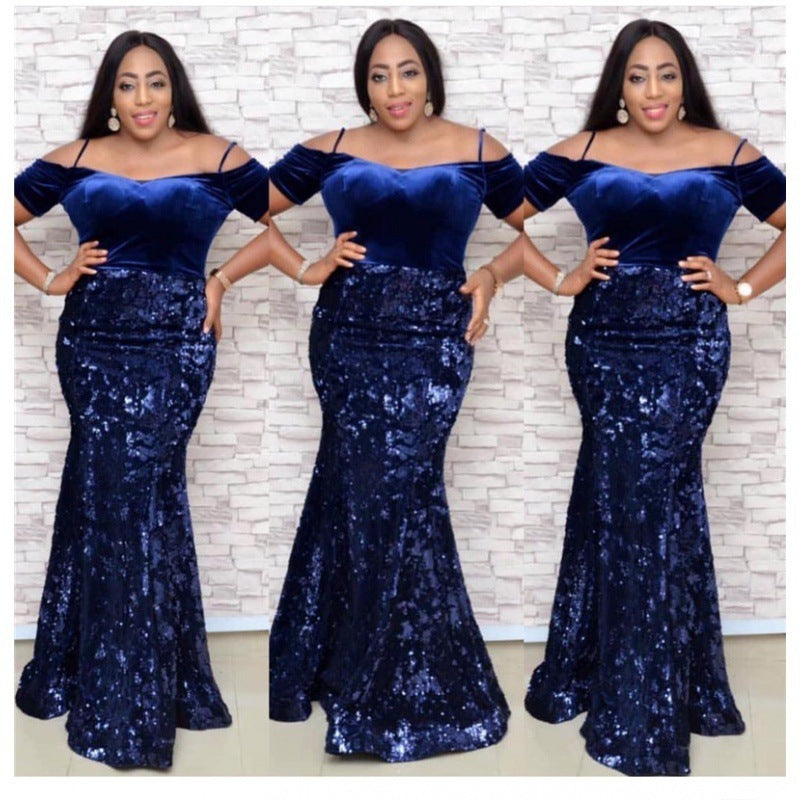 Woman wearing a blue off-shoulder gown with sequin skirt against a white brick wall.