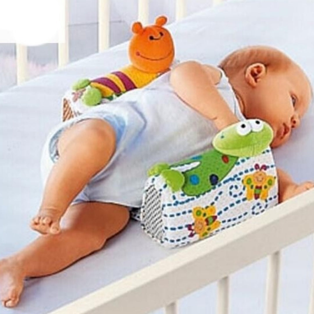 Baby lying on a wedge with toys in a crib
