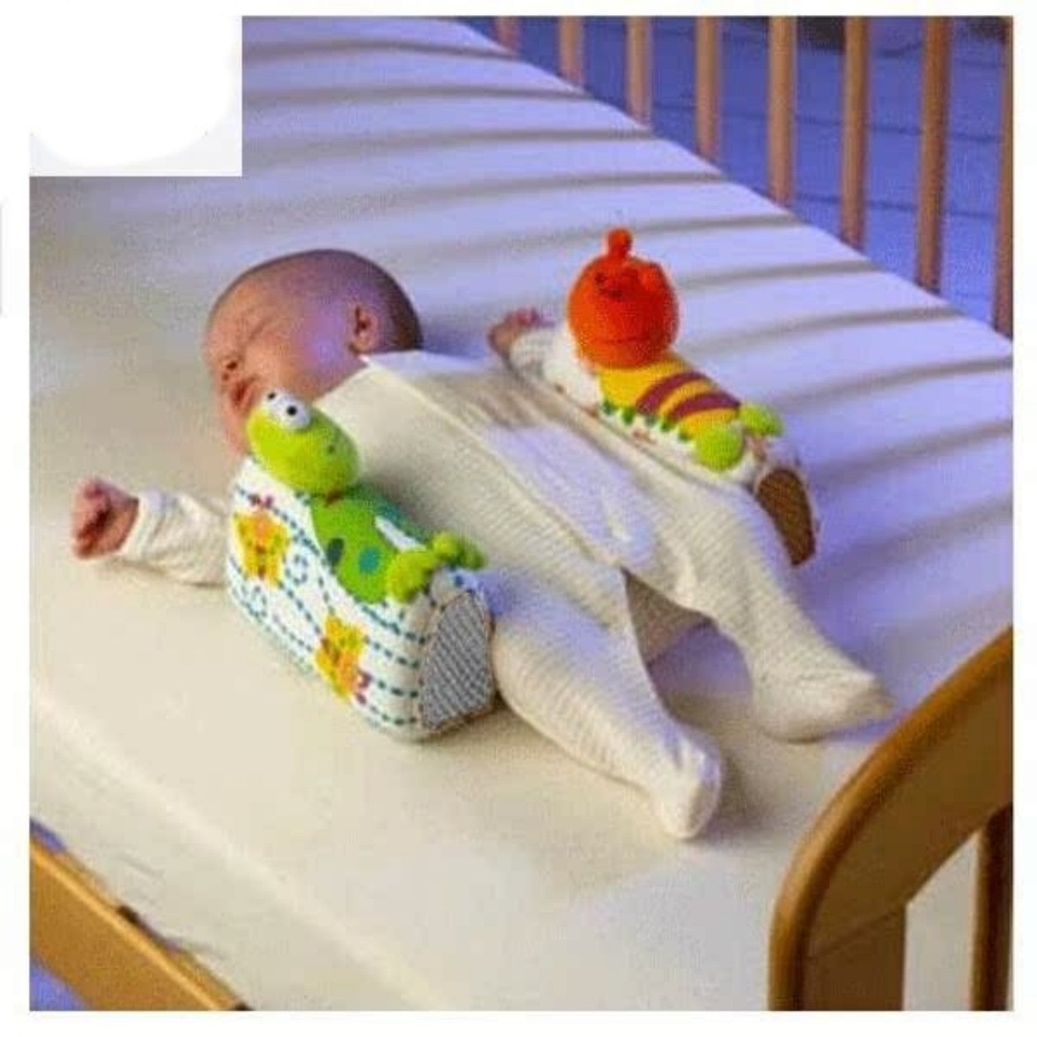 Baby lying on a crib with colorful caterpillar toys attached to its legs.