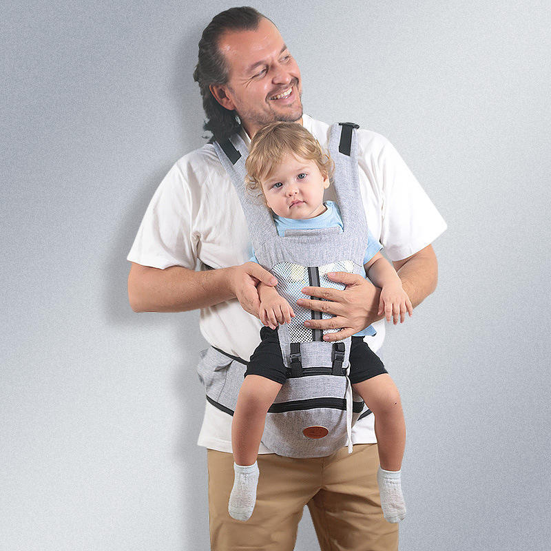 Man holding a child in a baby carrier against a plain background