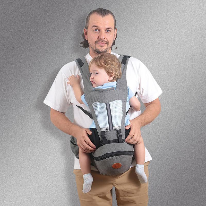 Man holding a child in a baby carrier against a gray background