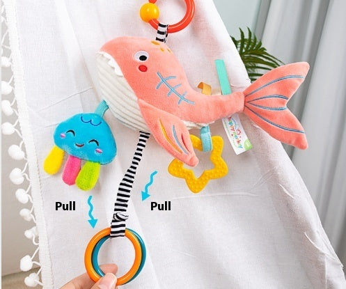 Colorful fish-shaped baby toy with pull tabs on a white fabric background