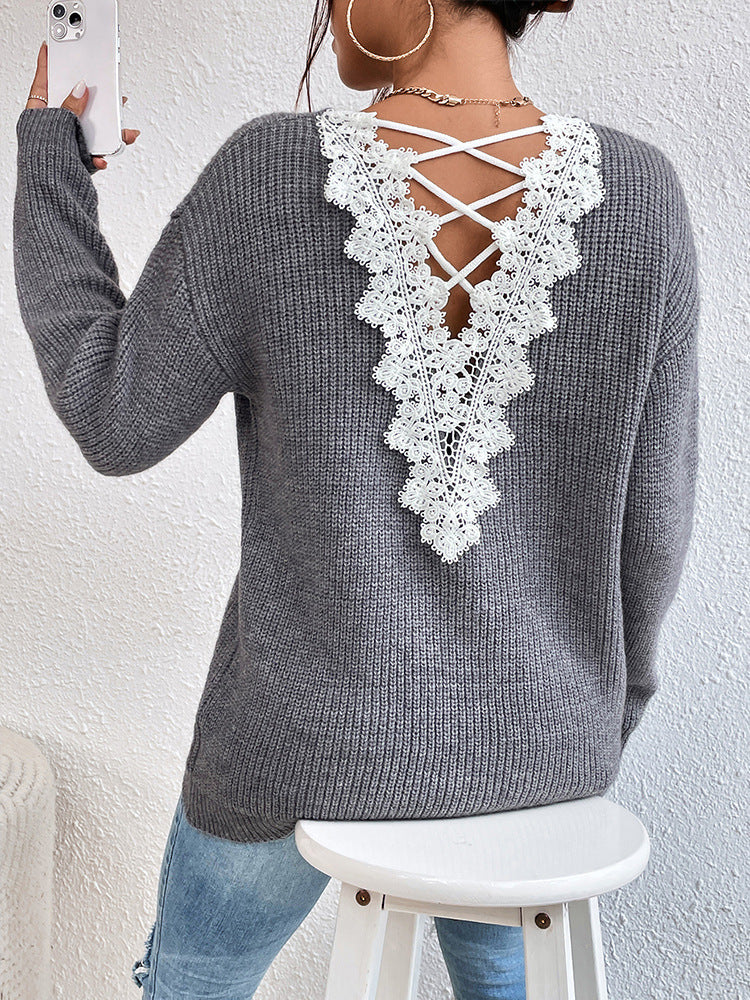 Gray sweater with white lace back design worn by a person, sitting on a white stool against a light gray wall.