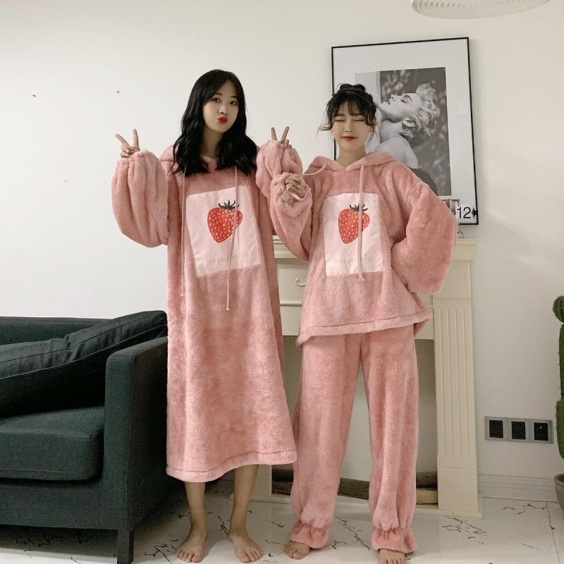 Two people wearing pink plush pajama sets with strawberry designs in a living room.