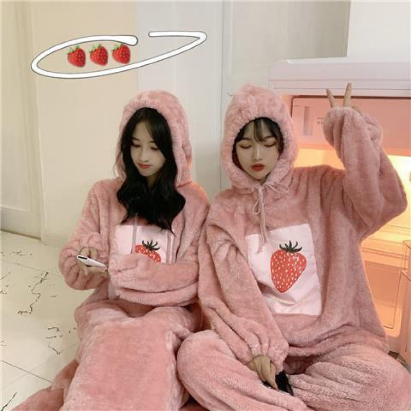 Two people wearing pink fleece onesies with strawberry designs in a room.