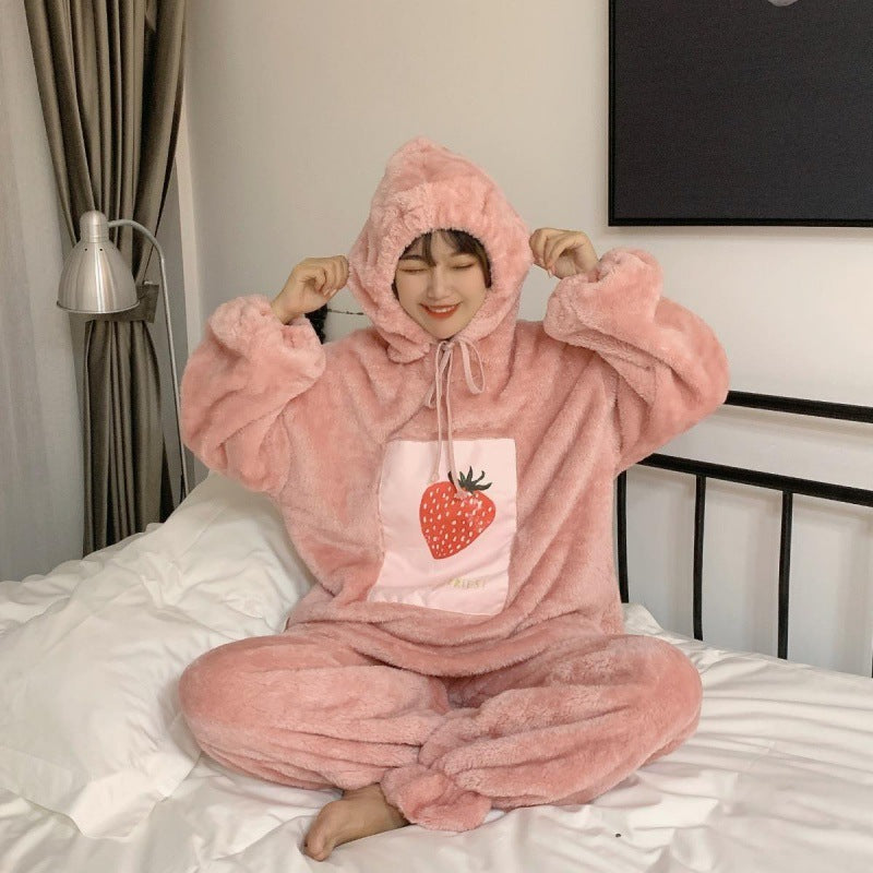 Person wearing a pink plush onesie with a strawberry design on a bed.