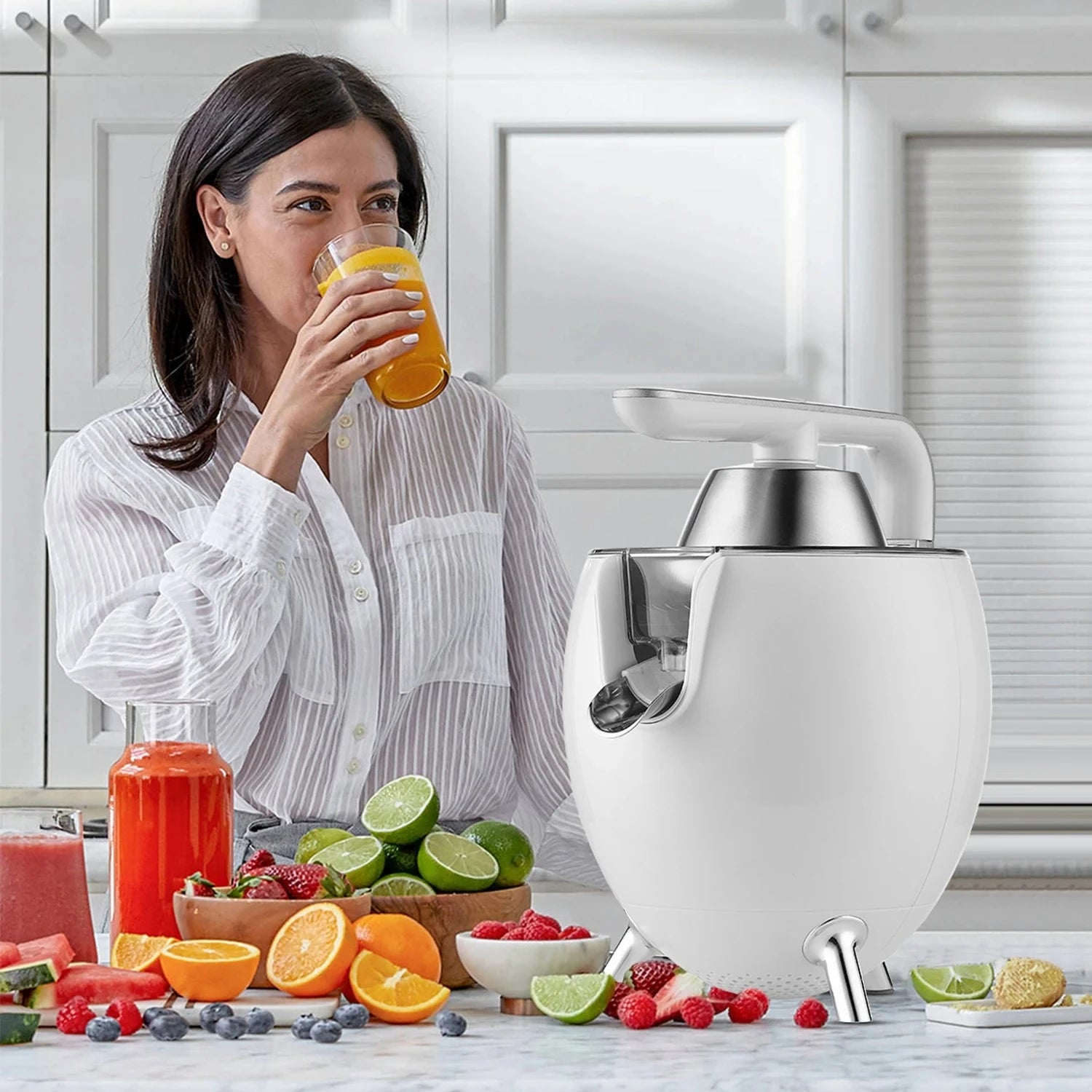 Woman drinking orange juice next to a blender with fruits on a kitchen counter