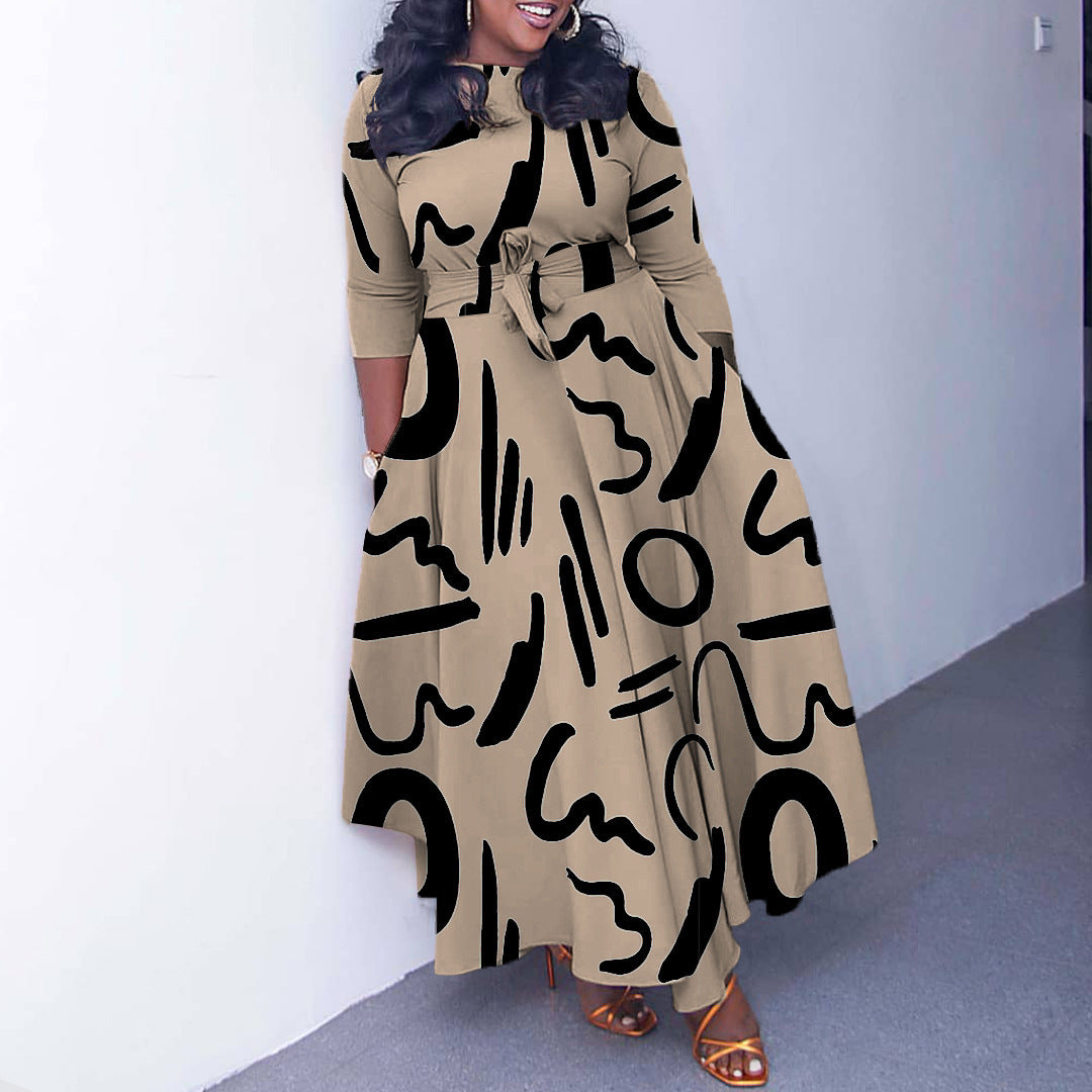 Woman wearing a long beige dress with black abstract patterns against a white wall.