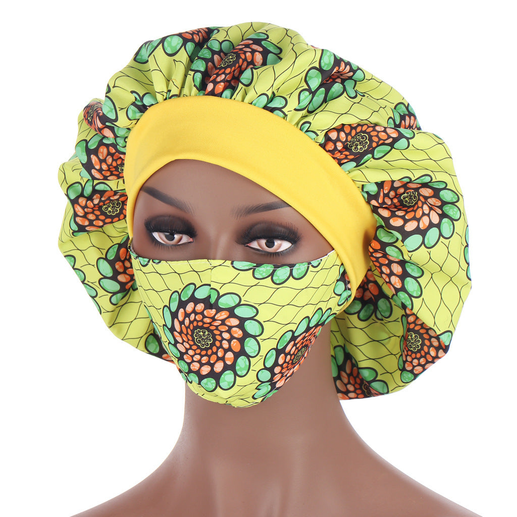 Mannequin head wearing a bright yellow and green patterned headscarf and face mask on a white background