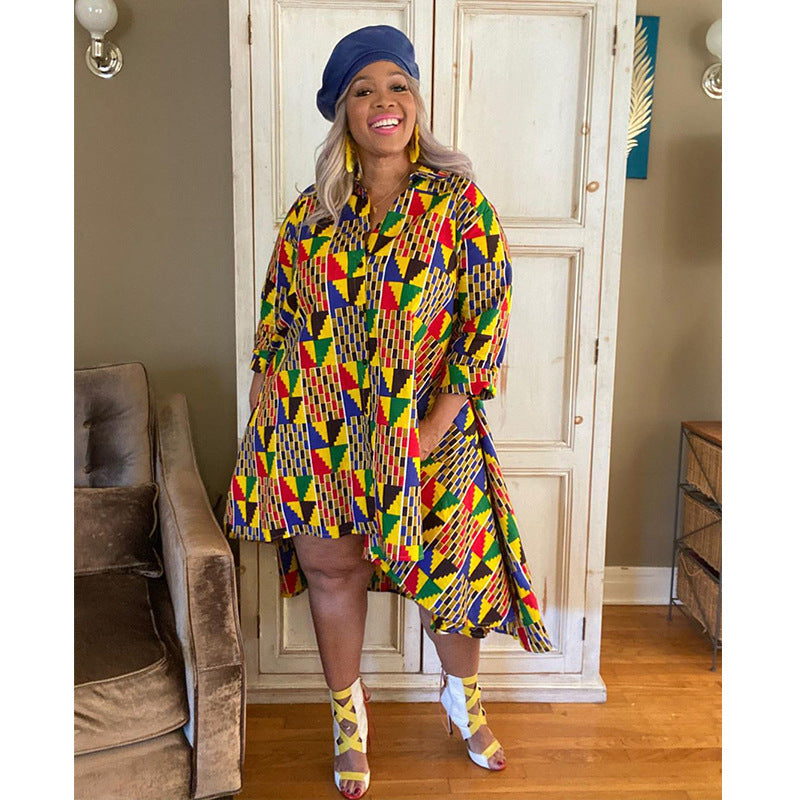 Woman in a colorful patterned dress standing in a room with a couch and door in the background.