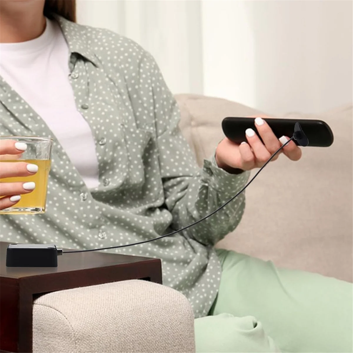 Person sitting on a couch holding a glass of beer and a remote control, with a neutral background.