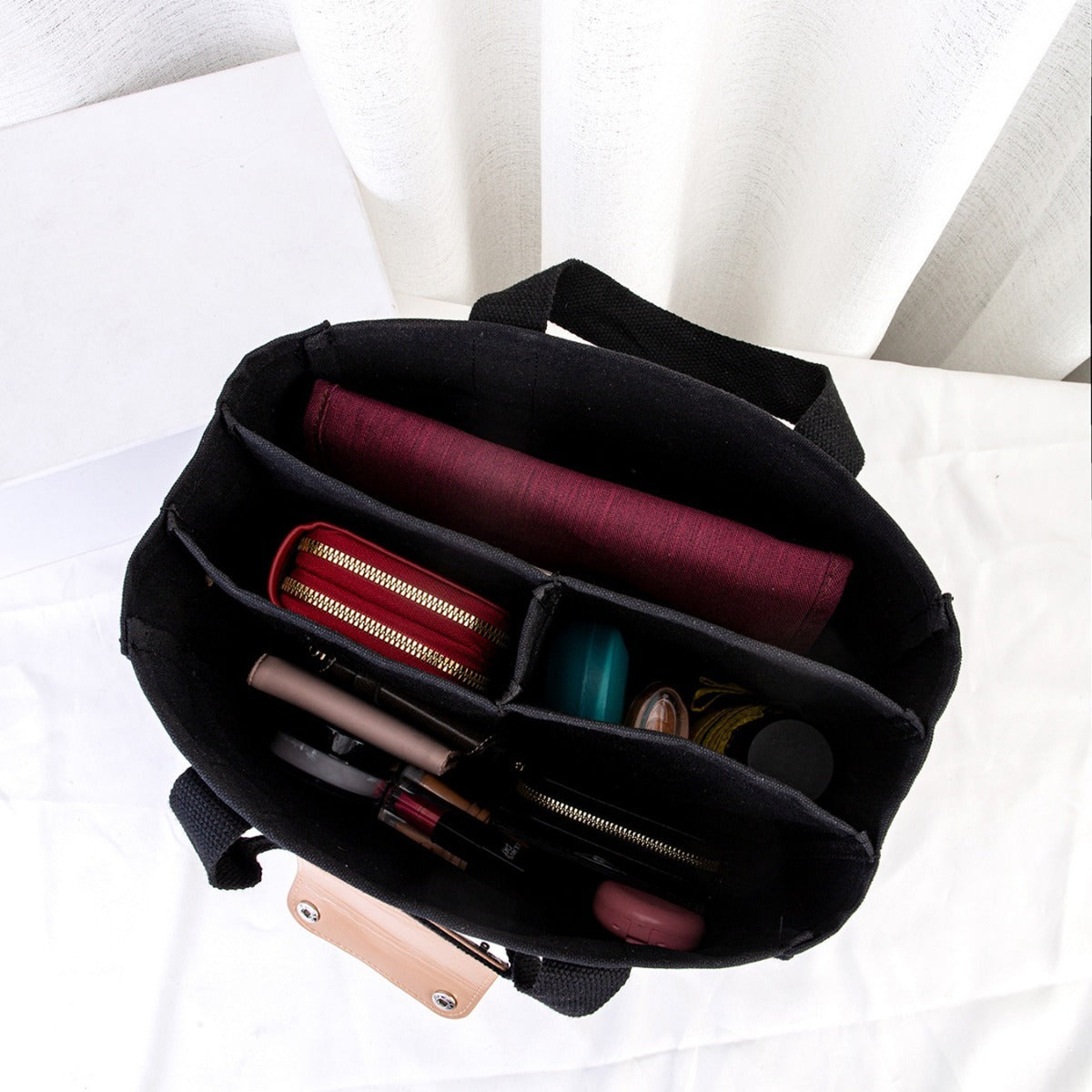Black handbag with makeup items on a white background