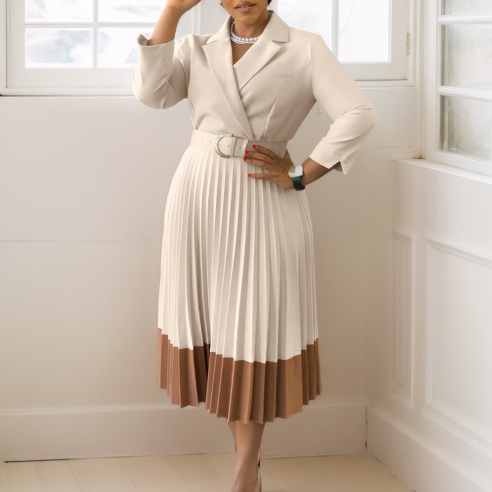 Person wearing a beige and brown dress with a belt in a room with white walls and a window.