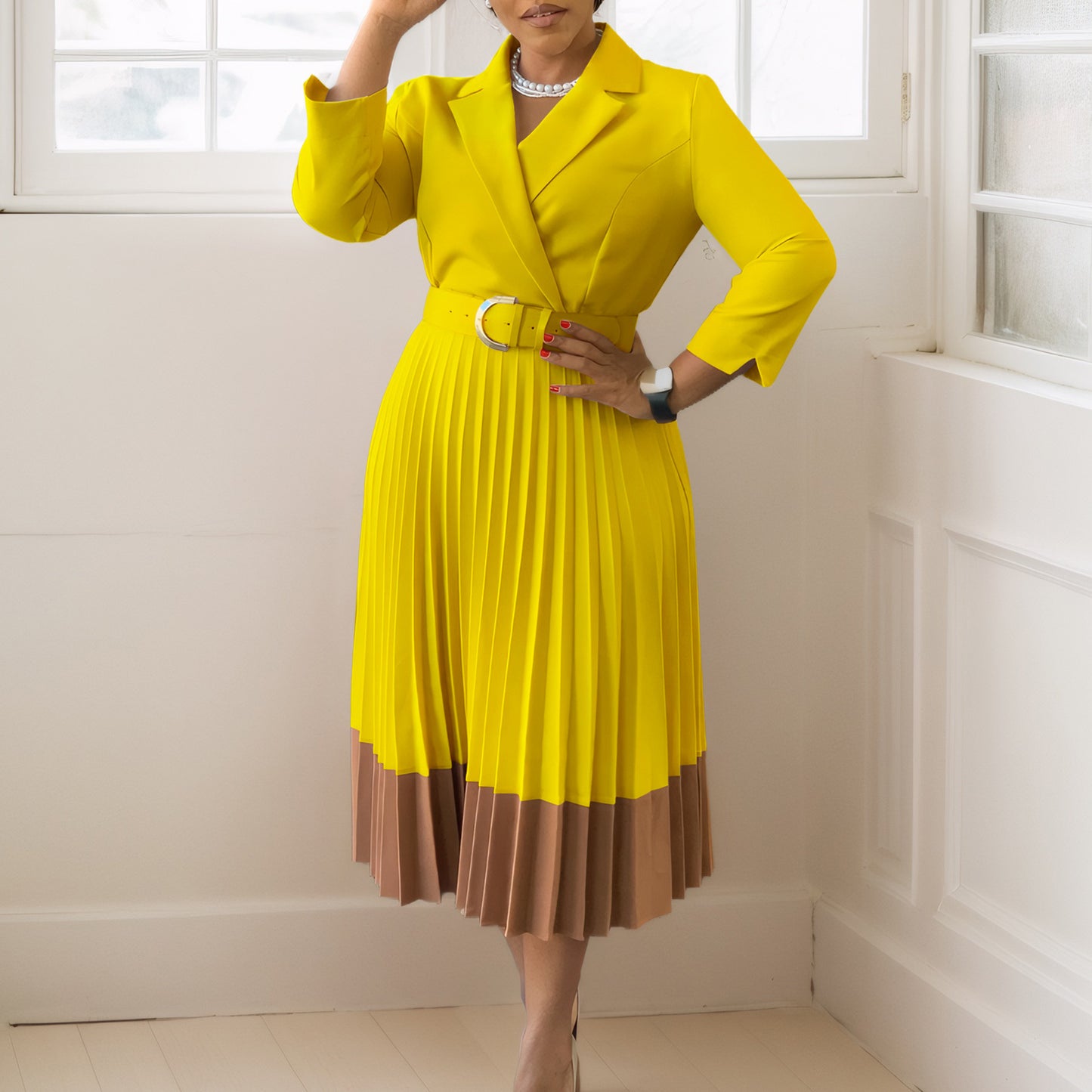 Woman wearing a yellow dress with a brown bottom section in a room with white walls.