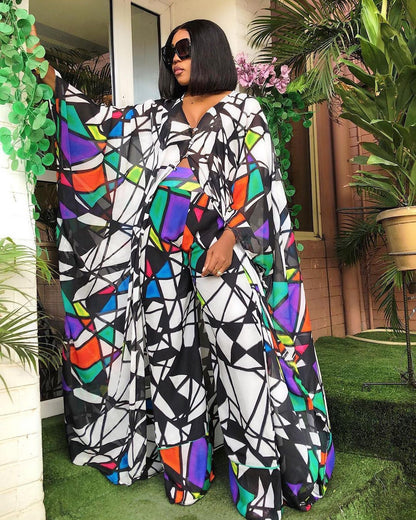 Woman wearing a colorful geometric patterned outfit standing outdoors with plants around.