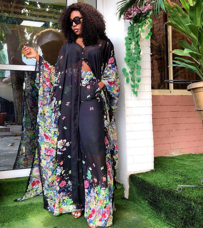 Woman in a black outfit with floral patterns standing outdoors.