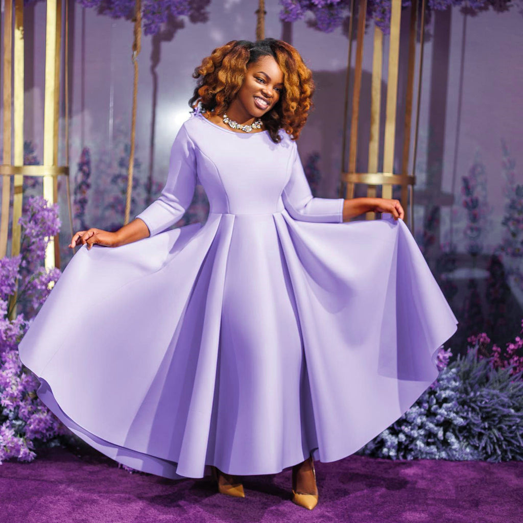 Woman in a long light purple dress standing in a decorated indoor setting with flowers.