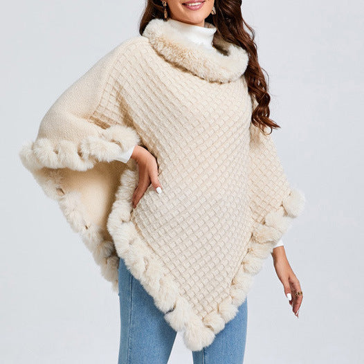 Woman wearing a cream-colored knitted poncho with fur trim on a plain background