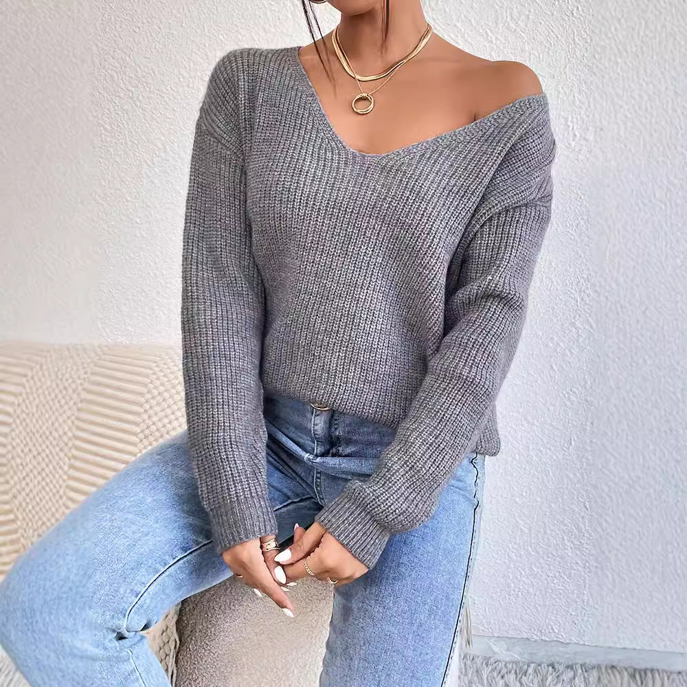 Person wearing a gray off-shoulder sweater and blue jeans against a white background