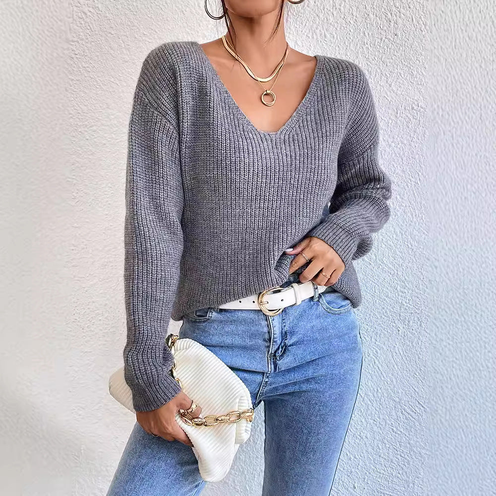 Person wearing a gray sweater and blue jeans with a white clutch against a light background