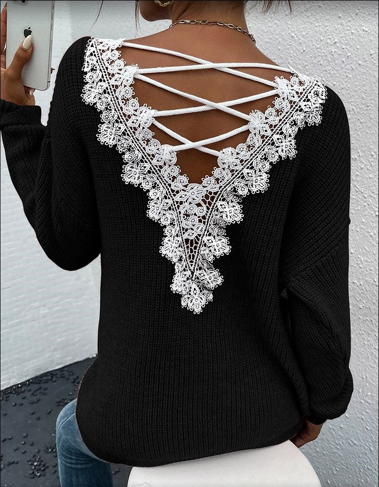 Black sweater with white lace detailing on the back against a light gray wall.