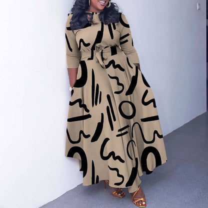 Woman wearing a long beige dress with black abstract patterns against a white wall.