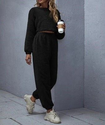 Person wearing a black outfit holding a coffee cup against a gray wall.
