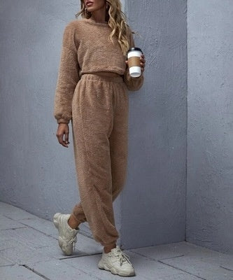 Woman wearing a brown knit outfit holding a coffee cup against a gray wall.