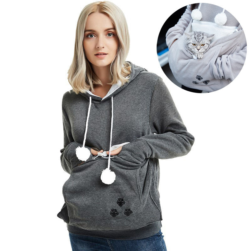 Woman wearing a gray hoodie with pom-pom details, inset showing a cat inside the hood.