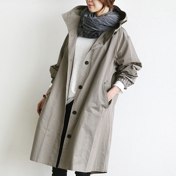 Person wearing a long gray coat with a hood on a plain background