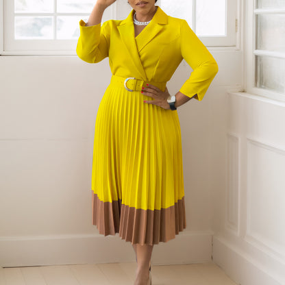 Woman wearing a yellow dress with a brown bottom section in a room with white walls.