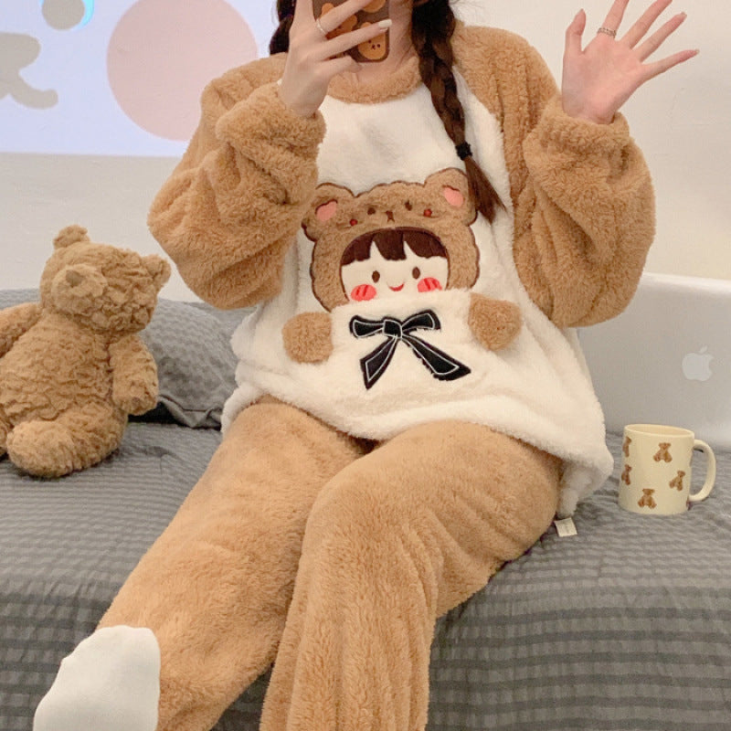 Person wearing a brown and white outfit with a cartoon design, sitting on a bed with a teddy bear and mug.