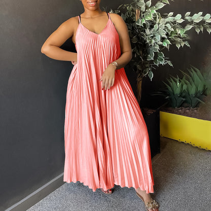 Woman wearing a pink pleated dress standing against a dark wall with plants.