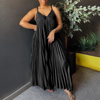 Woman wearing a black pleated dress standing against a dark wall with plants.