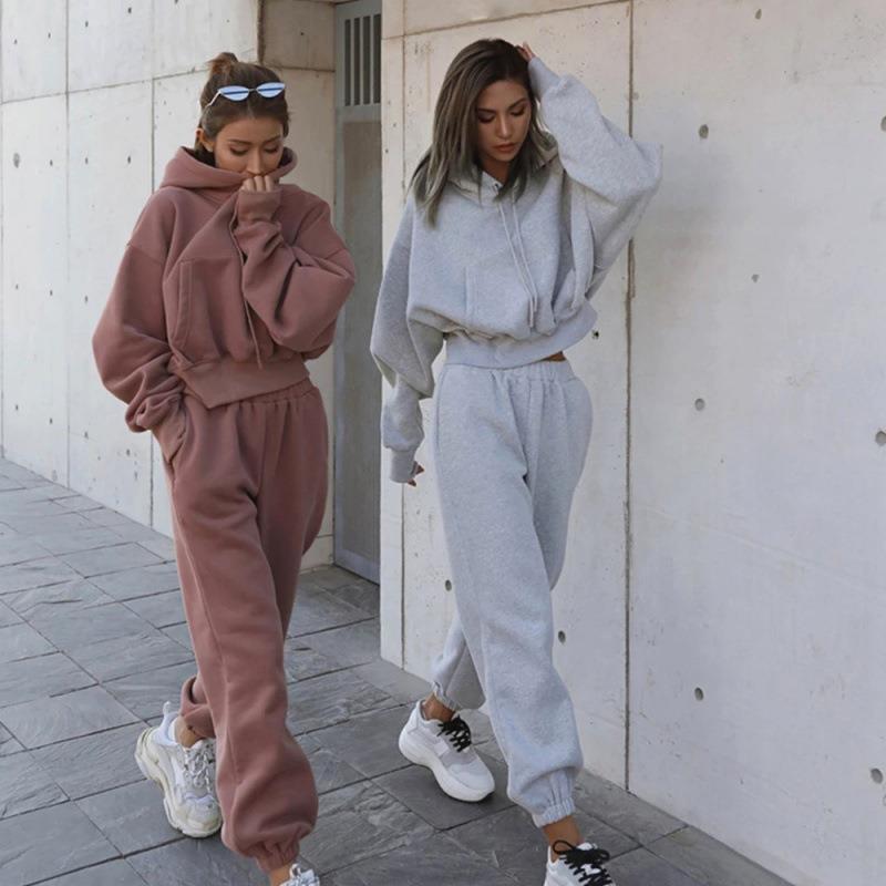 Two women wearing matching tracksuits standing against a white wall.