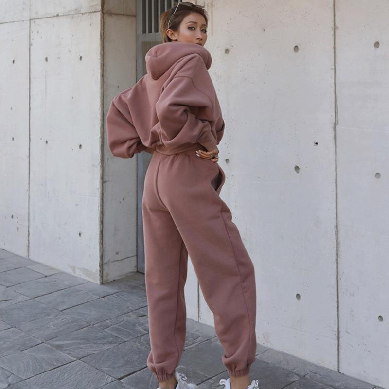Person wearing a pink tracksuit standing against a concrete wall.