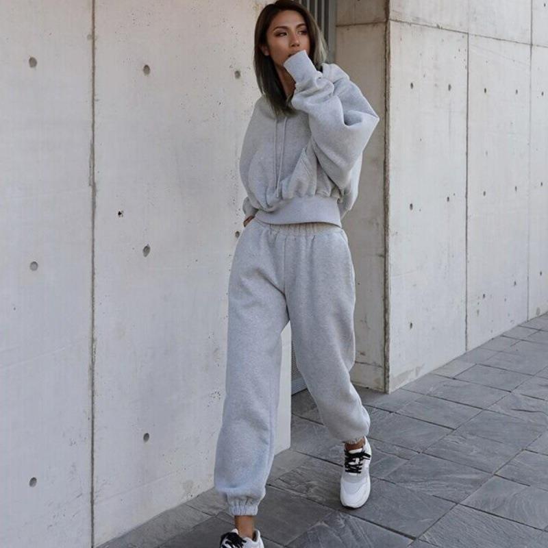 Person wearing a gray tracksuit standing against a concrete wall.